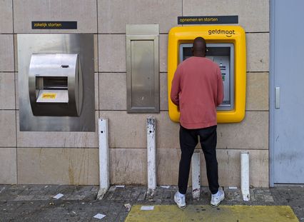 personne retirant des sous d'un DAB dans la rue installé à coté d'un appareil pour déposer de l'argent