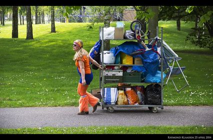 Femme en orange qui tire un énorme chario de 2m de haut plein de trucs et de sacs plastiques bleus cc-by-nd Raymond Klaassen